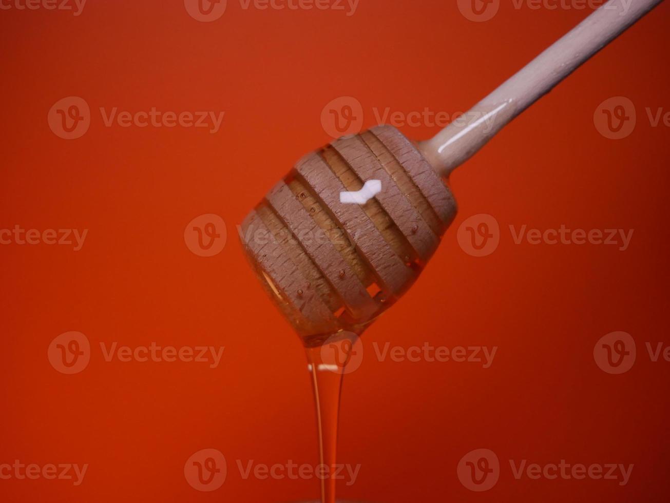 líquido miel en un huso cuchara en un naranja antecedentes foto