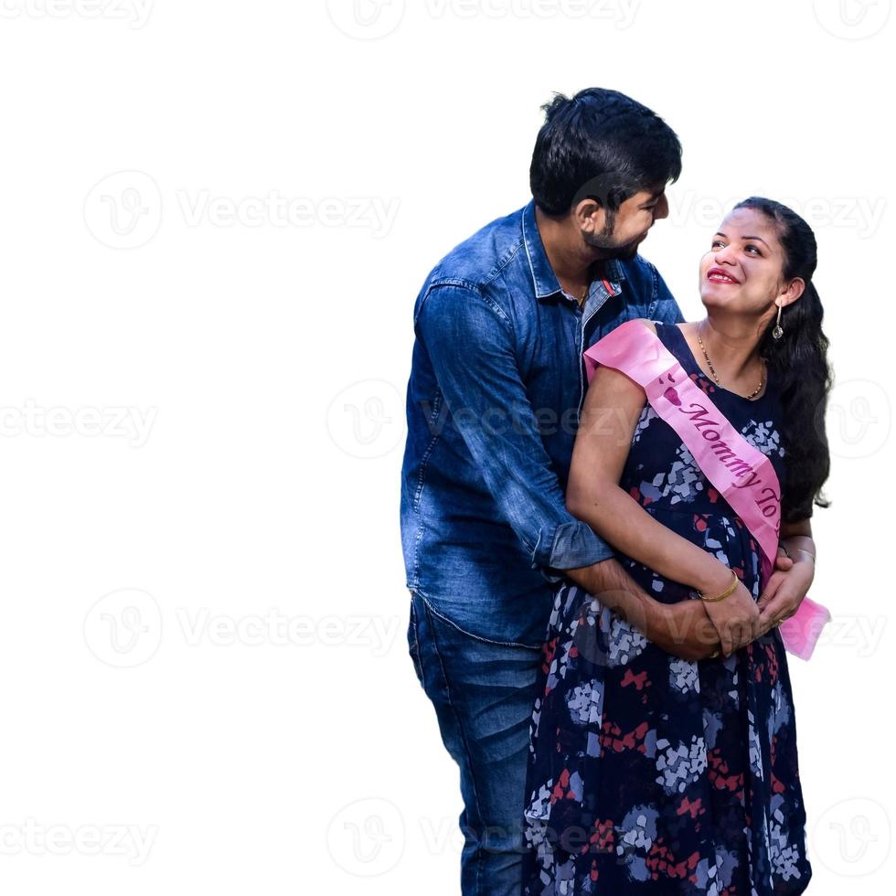 Indian couple posing for maternity baby shoot with white plain background. The couple is posing in a lawn with green grass and the woman is falunting her baby bump in Lodhi Garden in New Delhi, India photo