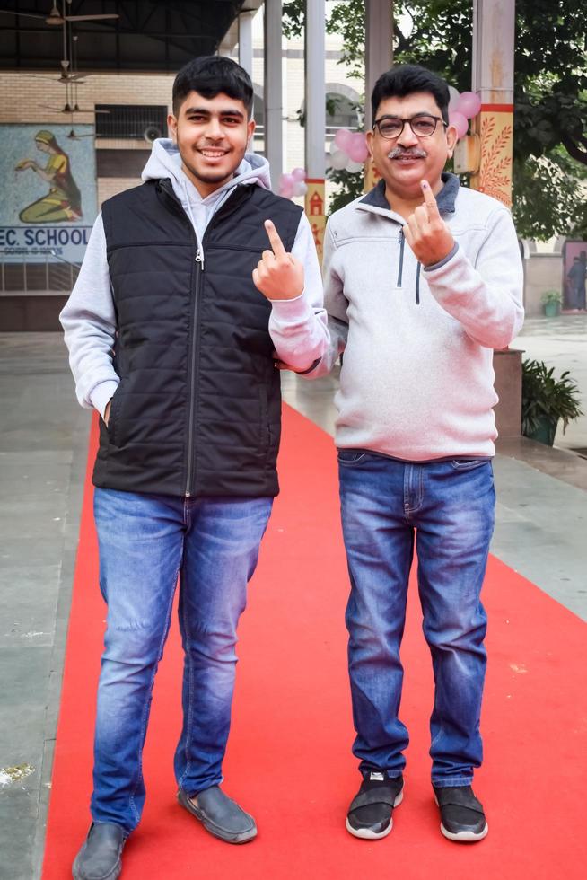 New Delhi, India - December 04 2022 - Unidentified people showing their ink-marked fingers after casting votes in front of polling booth of east Delhi area for MCD local body Elections 2022 photo