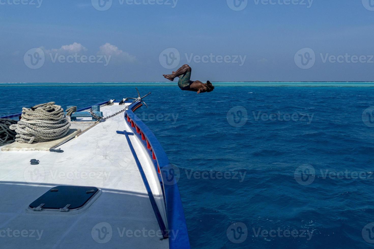 maldivian man jumping in water and diving from boat photo