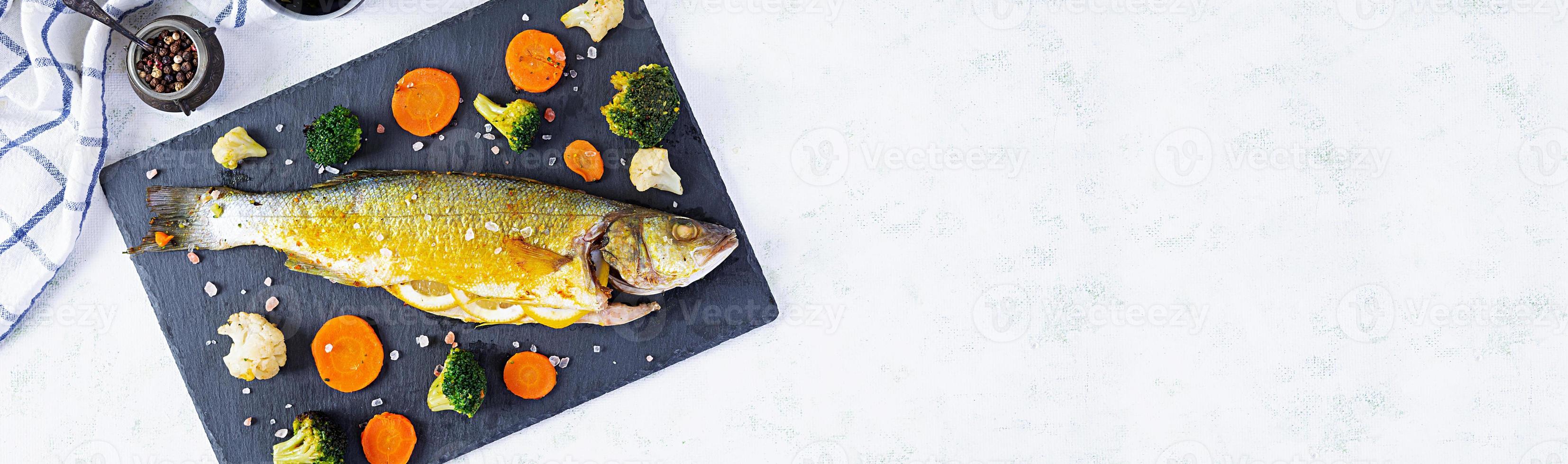 Baked sea bass fish with vegetables and greens on stone plate photo