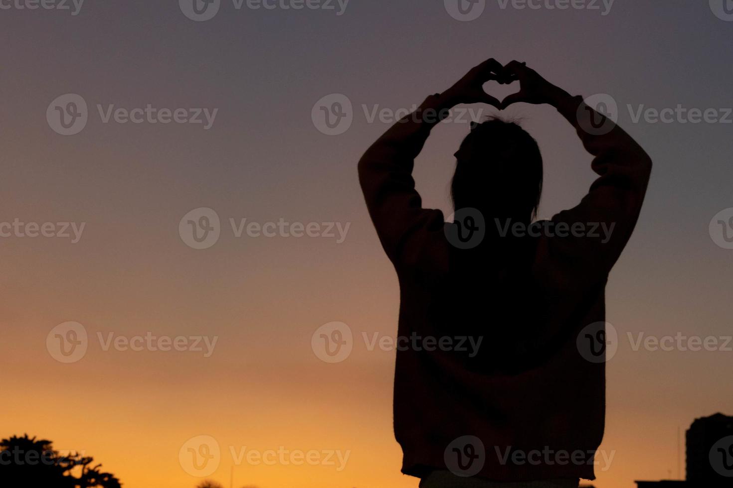 un silueta de un joven mujer levantamiento su manos encima su cabeza a representar un corazón símbolo significando amistad, amor y amabilidad. corazón símbolo concepto con el sentido de amor y amistad. foto