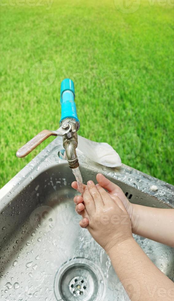 The boy's hands are washing their hands in the sink. There is a grass background. prevent germs photo