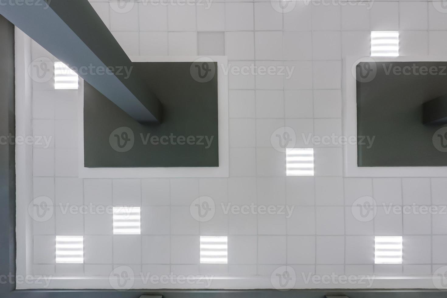 cassette stretched or suspended ceiling with square halogen spots lamps and drywall construction in empty room in house or office with column. Looking up view photo