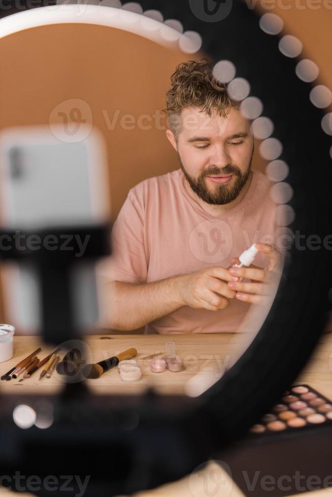 Man recording video vlog while applying cosmetics or explore cosmetic product. Guy making tutorial make-up for his blog on cosmetics. photo
