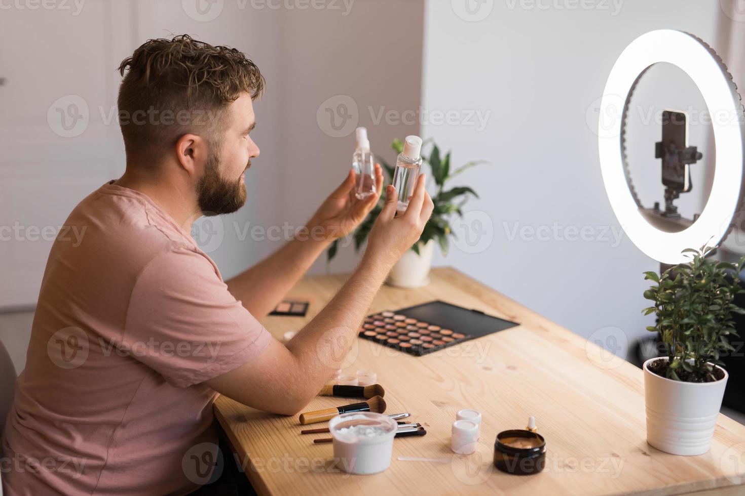 Man recording video vlog while applying cosmetics or explore cosmetic product. Guy making tutorial make-up for his blog on cosmetics. photo