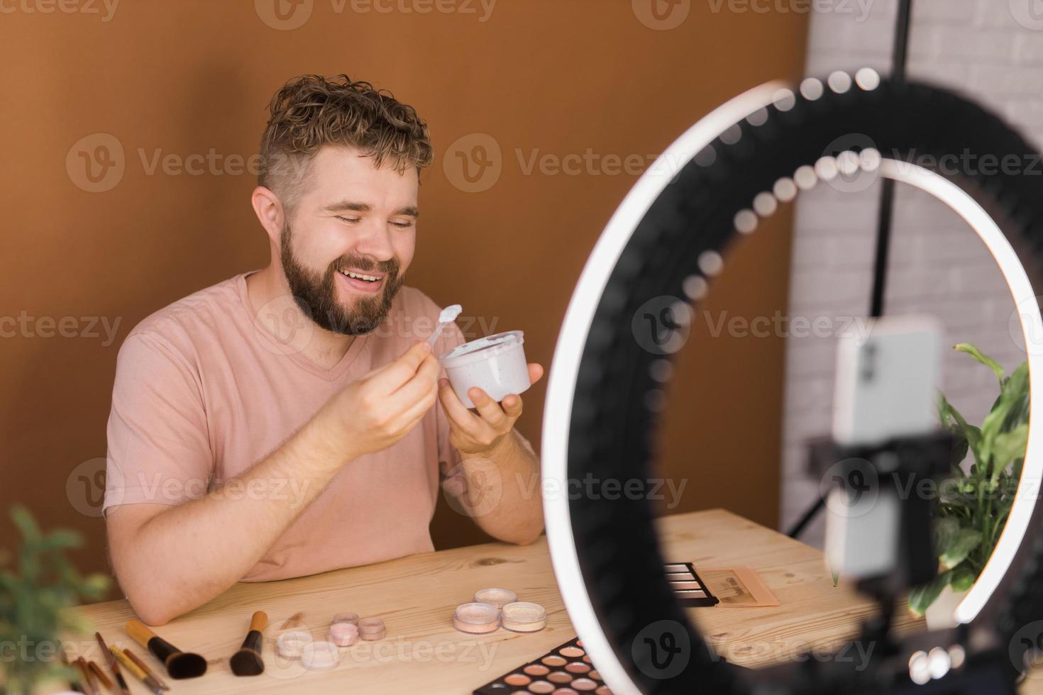 Man recording video vlog while applying cosmetics or explore cosmetic product. Guy making tutorial make-up for his blog on cosmetics. photo