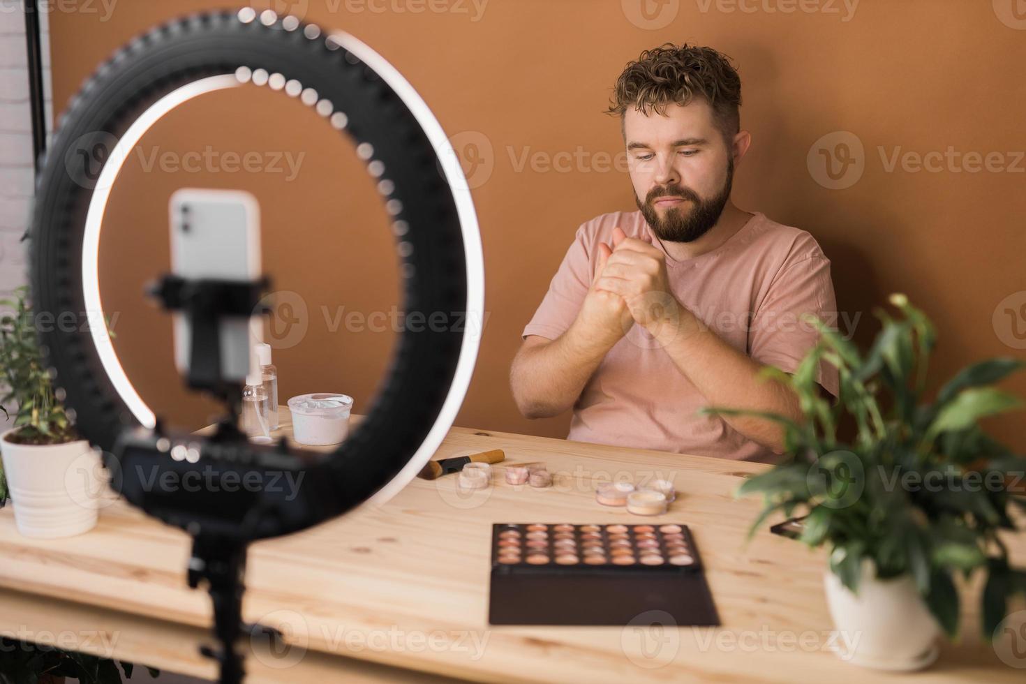 Man vlogging about make up and beauty products. Male shooting a makeup tutorial. Guy teaching make up tutorial using her phone - diversity and blogger concept. photo