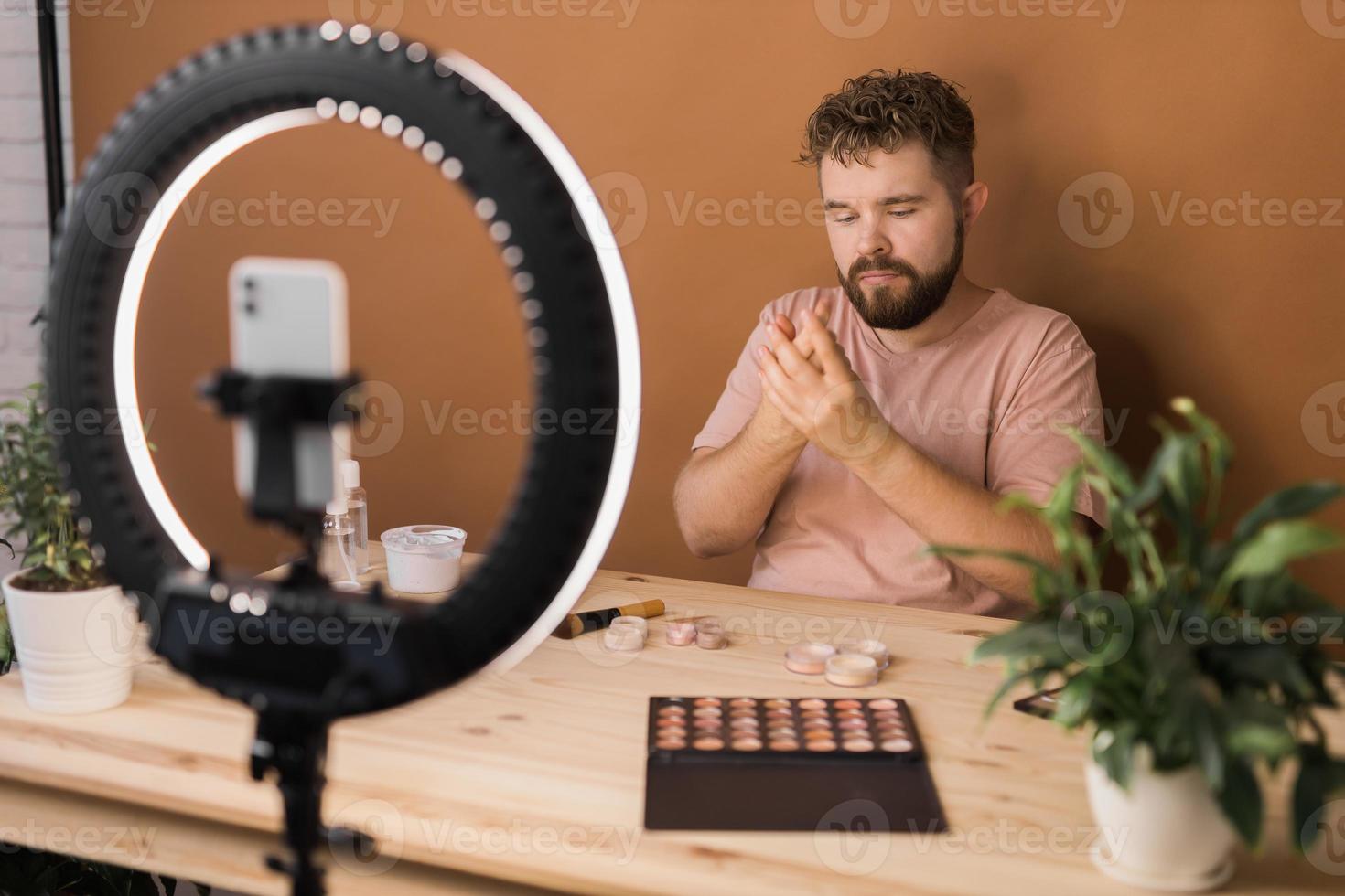 Male beauty blogger doing his make up and recording a video lesson his with mobile phone - vlog, diversity and video blog concept photo