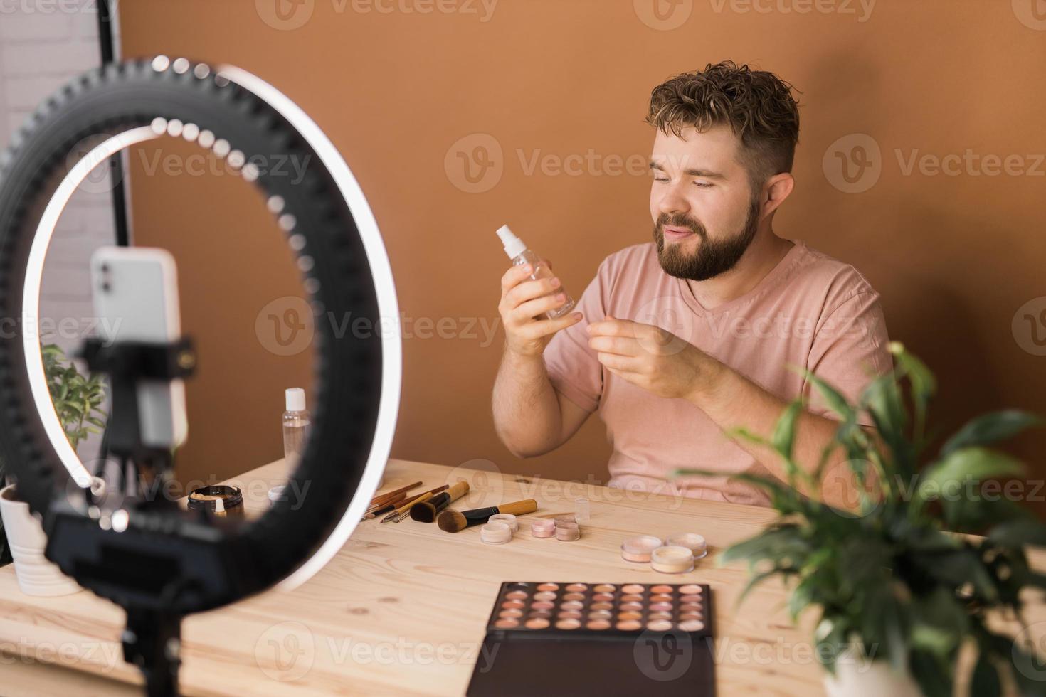Man recording video vlog while applying cosmetics or explore cosmetic product. Guy making tutorial make-up for his blog on cosmetics. photo