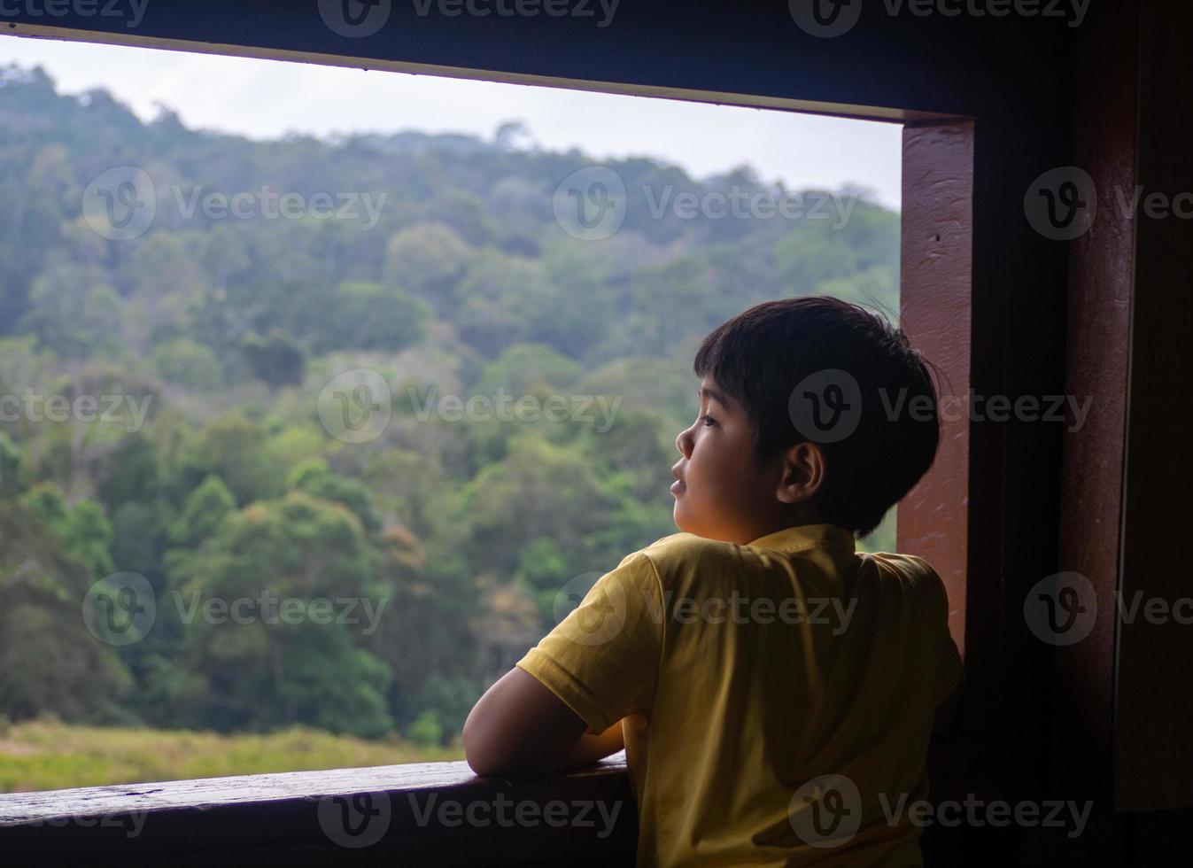 niño mirando por la ventana mirando el bosque verde foto