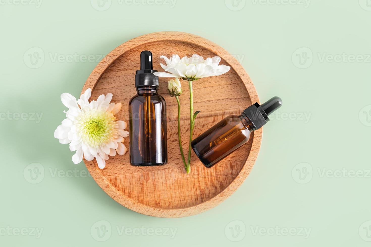 Two cosmetic bottles with an organic natural self-care pipette lie on a round wooden tray with white flowers. top view. green background. photo