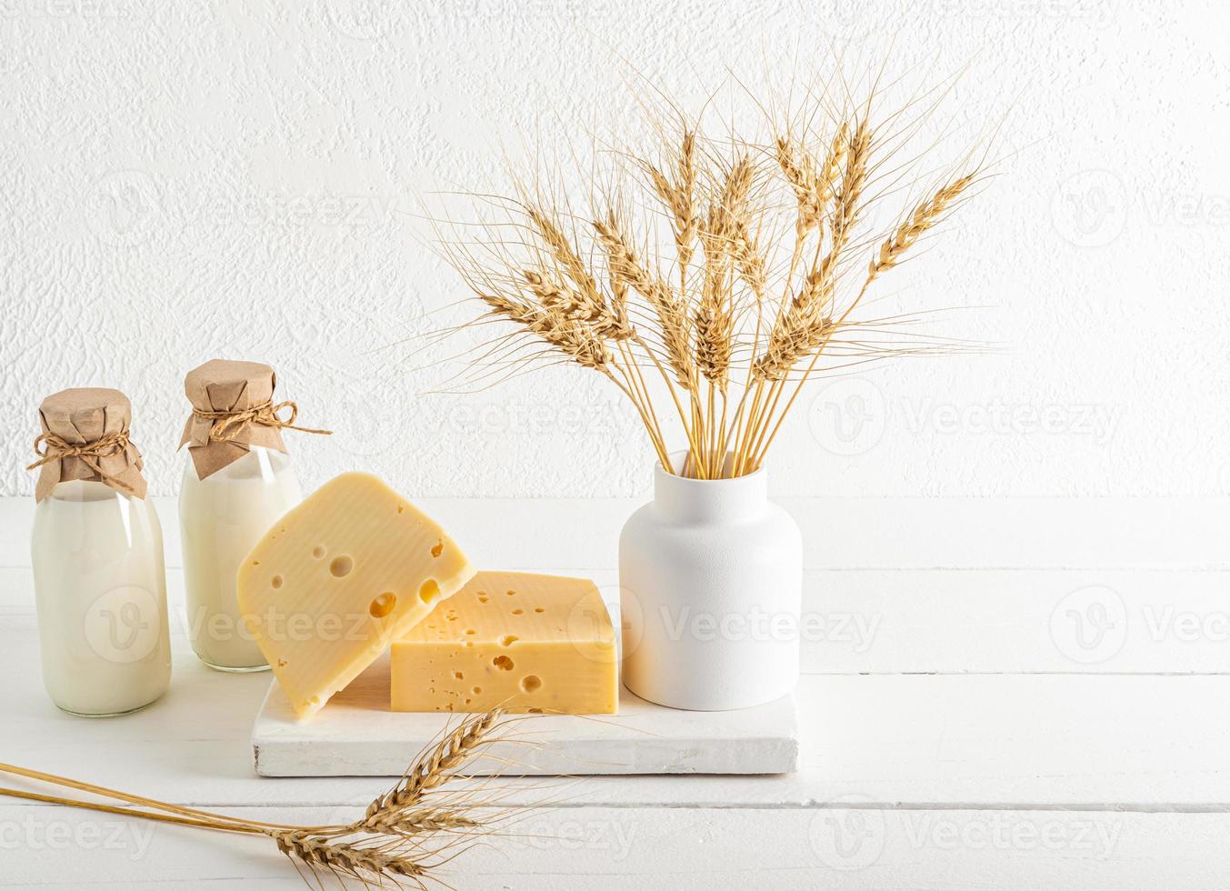 two bottles of fresh milk, two pieces of cheese on a white wooden podium. white background. minimalism. the concept of shavuot. photo
