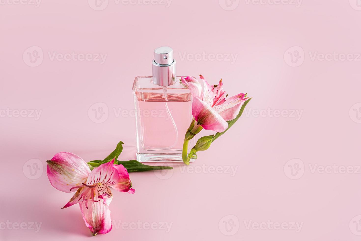 a bottle of perfume or cosmetic spray on a pink background with astromeria flowers. the concept of advertising a natural fragrance. a copy space. photo
