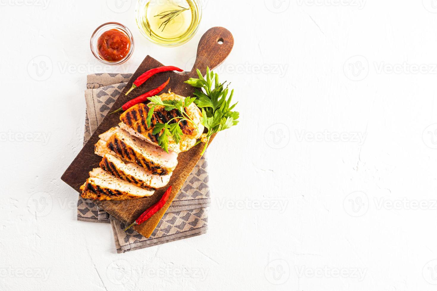 top view of freshly cooked grilled chicken fillets, portioned pieces. served on a cutting wooden board with fresh vegetables. a copy space. photo