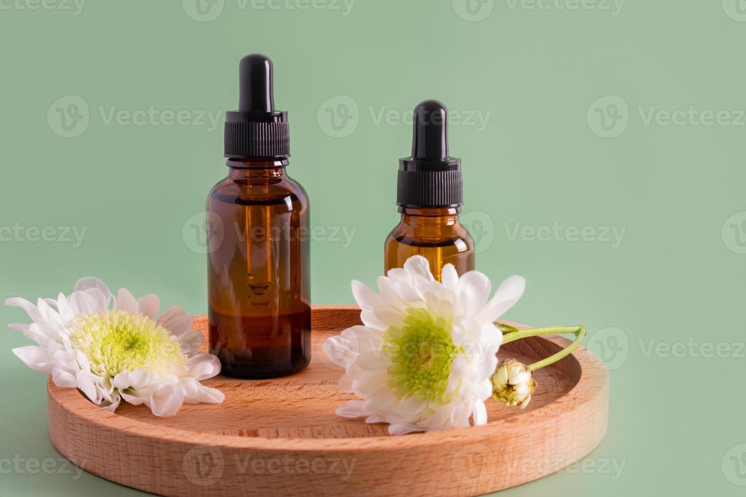 two bottles with a dropper with a natural remedy or serum for organic skin care of the face stand on a wooden plate. front view. green background. photo