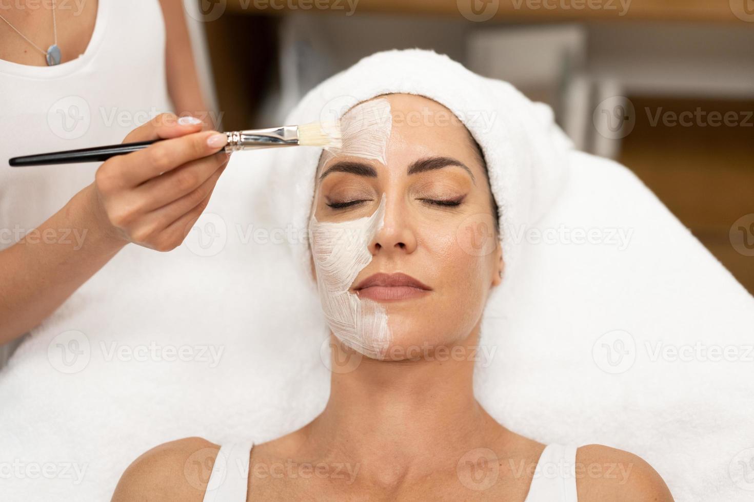 Aesthetics applying a mask to the face of a Middle-aged woman in modern wellness center. photo