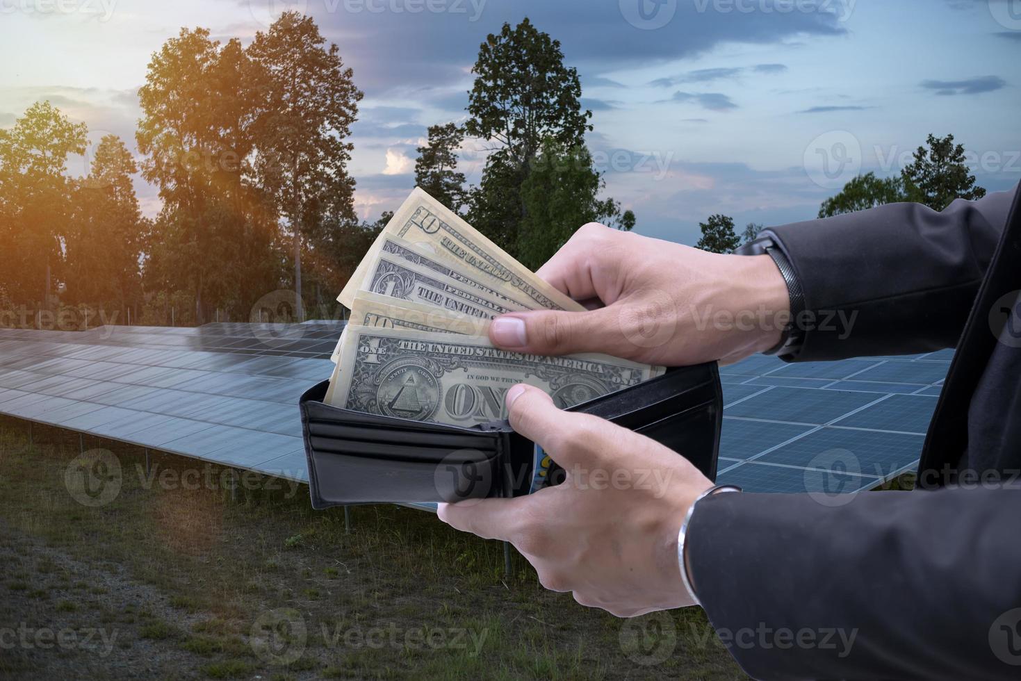 hand holding dollar bills that look out of a wallet on a background of solar panels. saves money. using solar energy. green electricity. photo