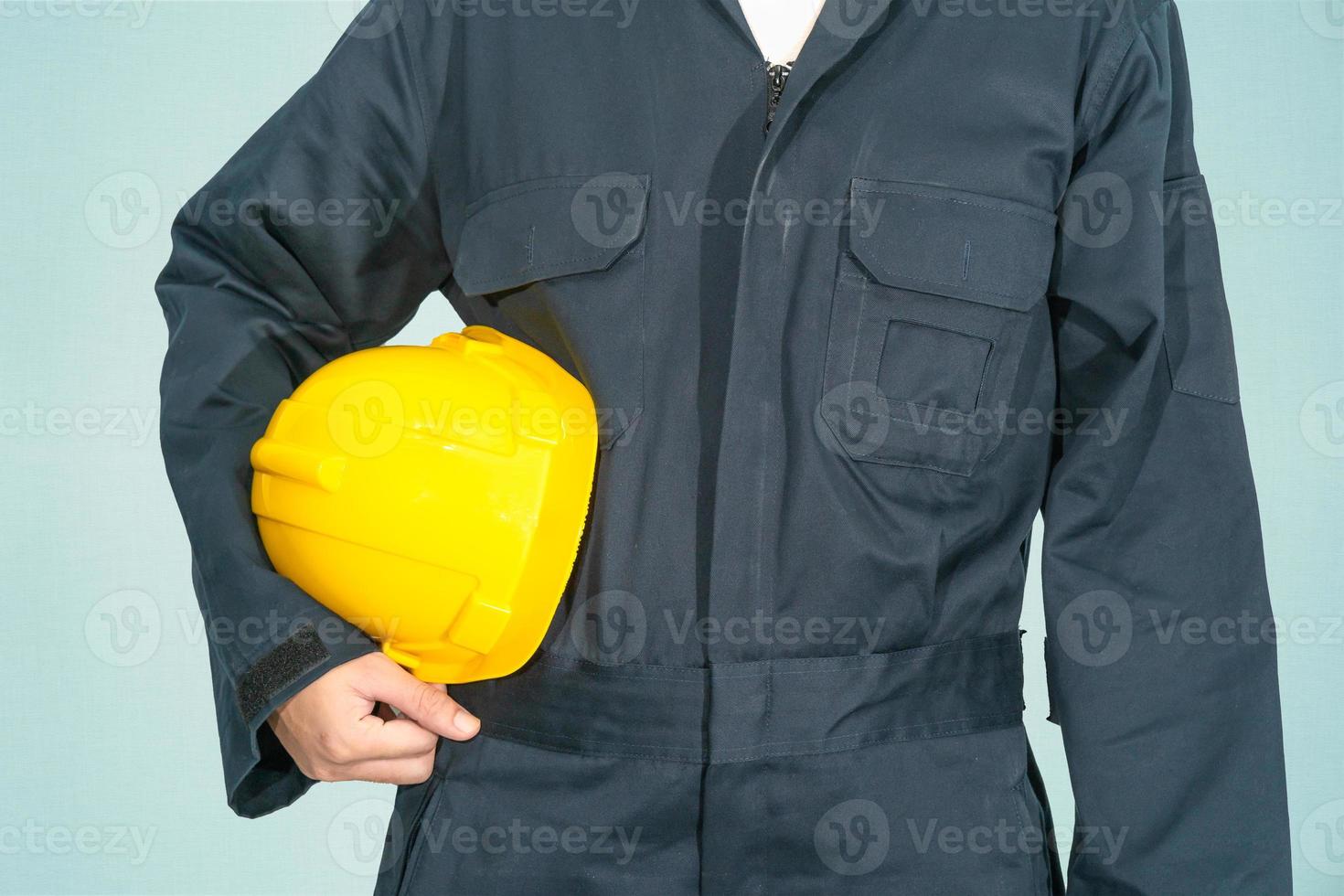 Worker standing in blue coverall holding yellow hardhat photo