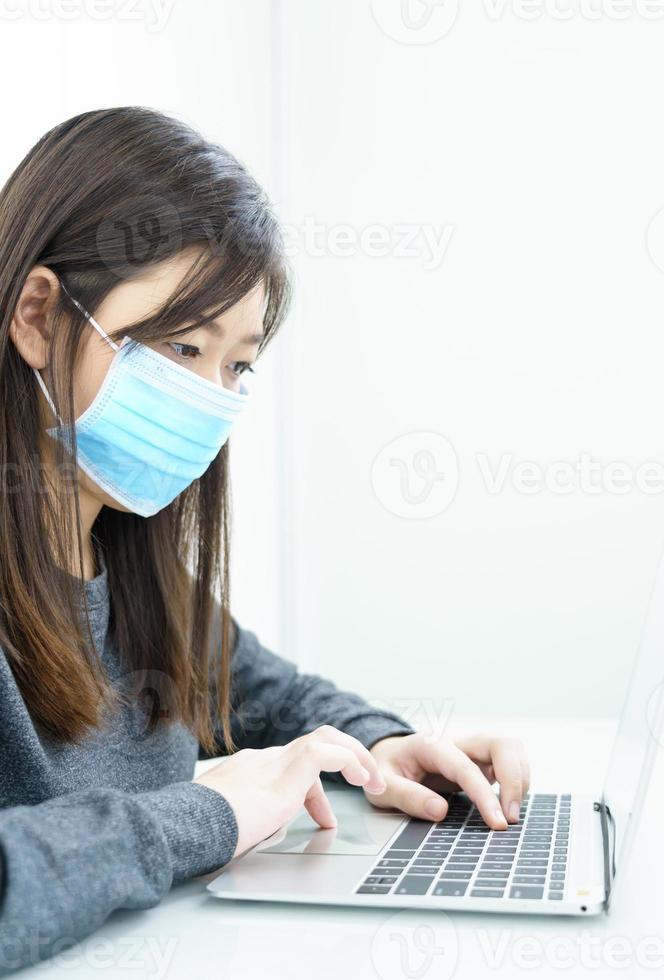 Woman using laptop on desk at home with wearing mask for protect Covid-19 photo