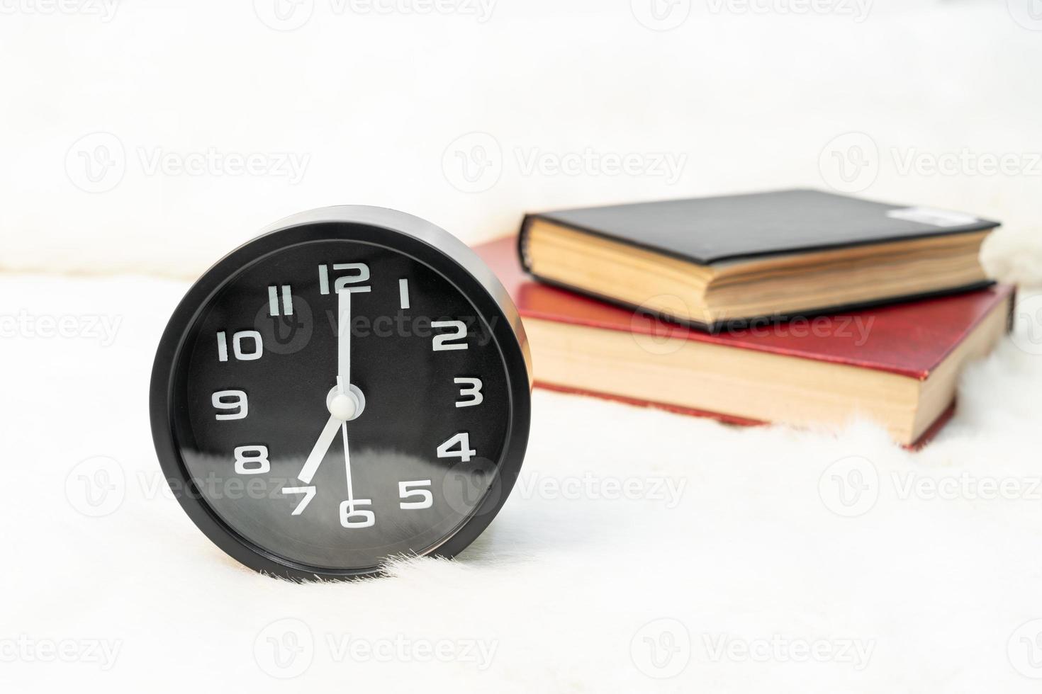 Black alarm clock and book stacked on table photo