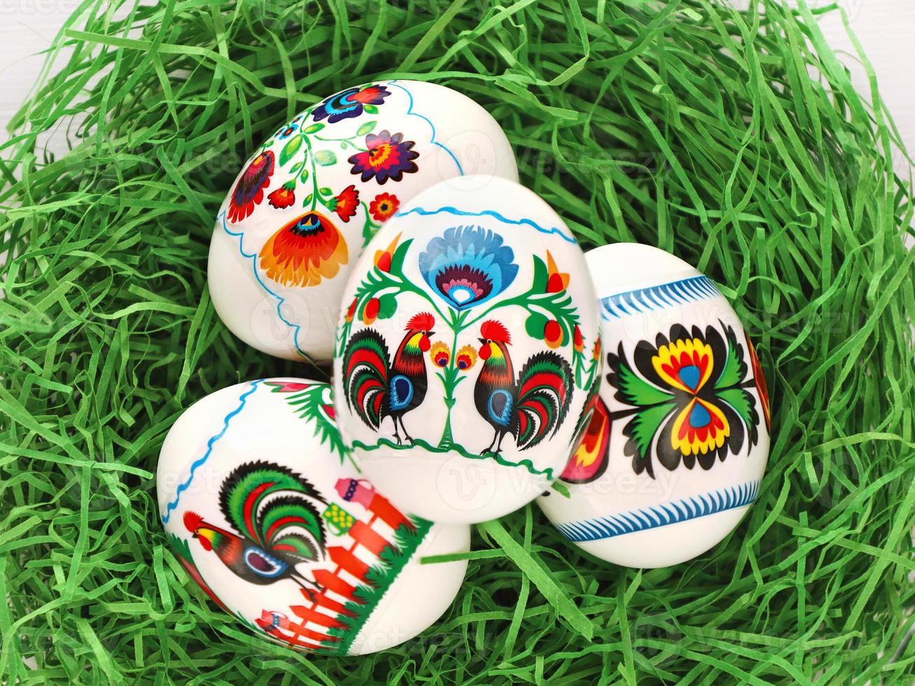 Four Colourful Easter Eggs with polish folk art motives thermal stickers in green paper grass nest. Polish traditional paper-cut with flowers and roosters from Lowicz region photo