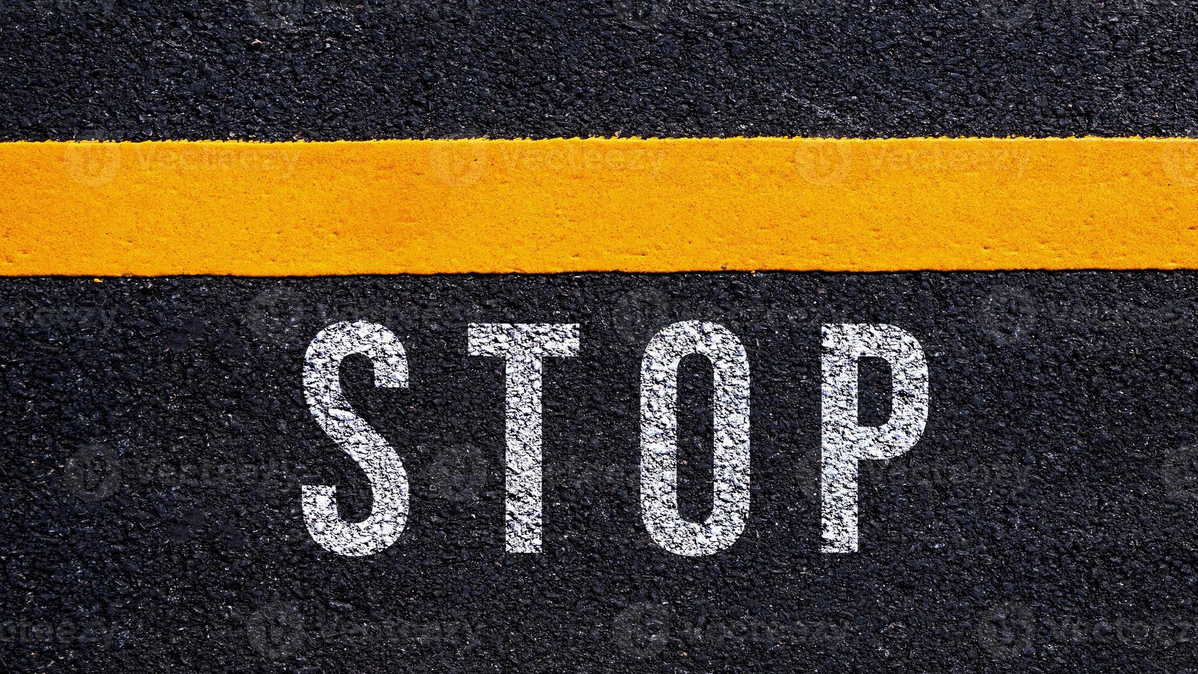 Stop text written and yellow line on the road in middle of the asphalt road, Stop word on street. photo