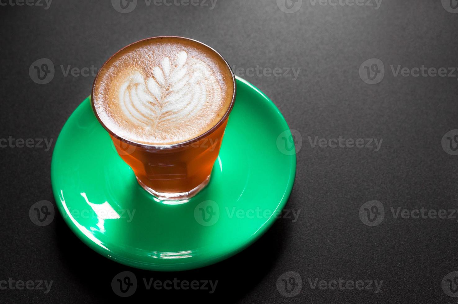 Hot latte in orange and green cup with floral pattern in foam on a dark background photo