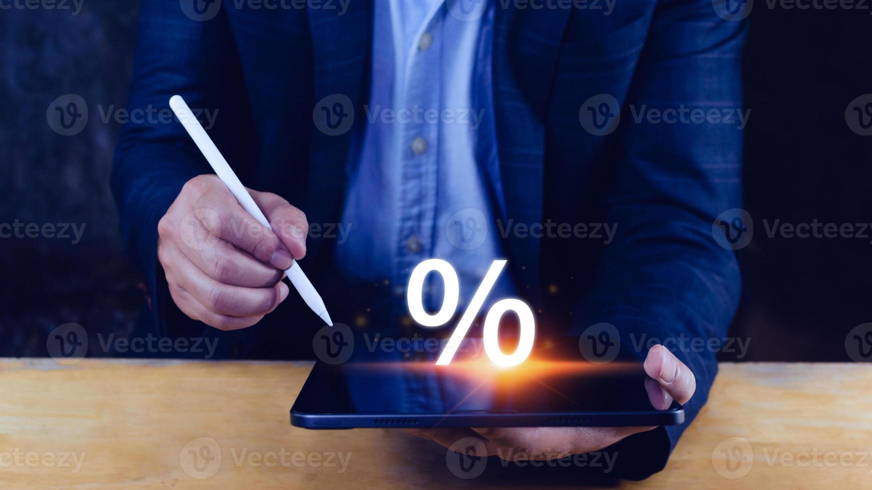 Businessman holding stylus pencil connection tablet display with percentage sign, monetary growth, interest rate increase, inflation concept, Interest rate financial and mortgage rates concept. photo