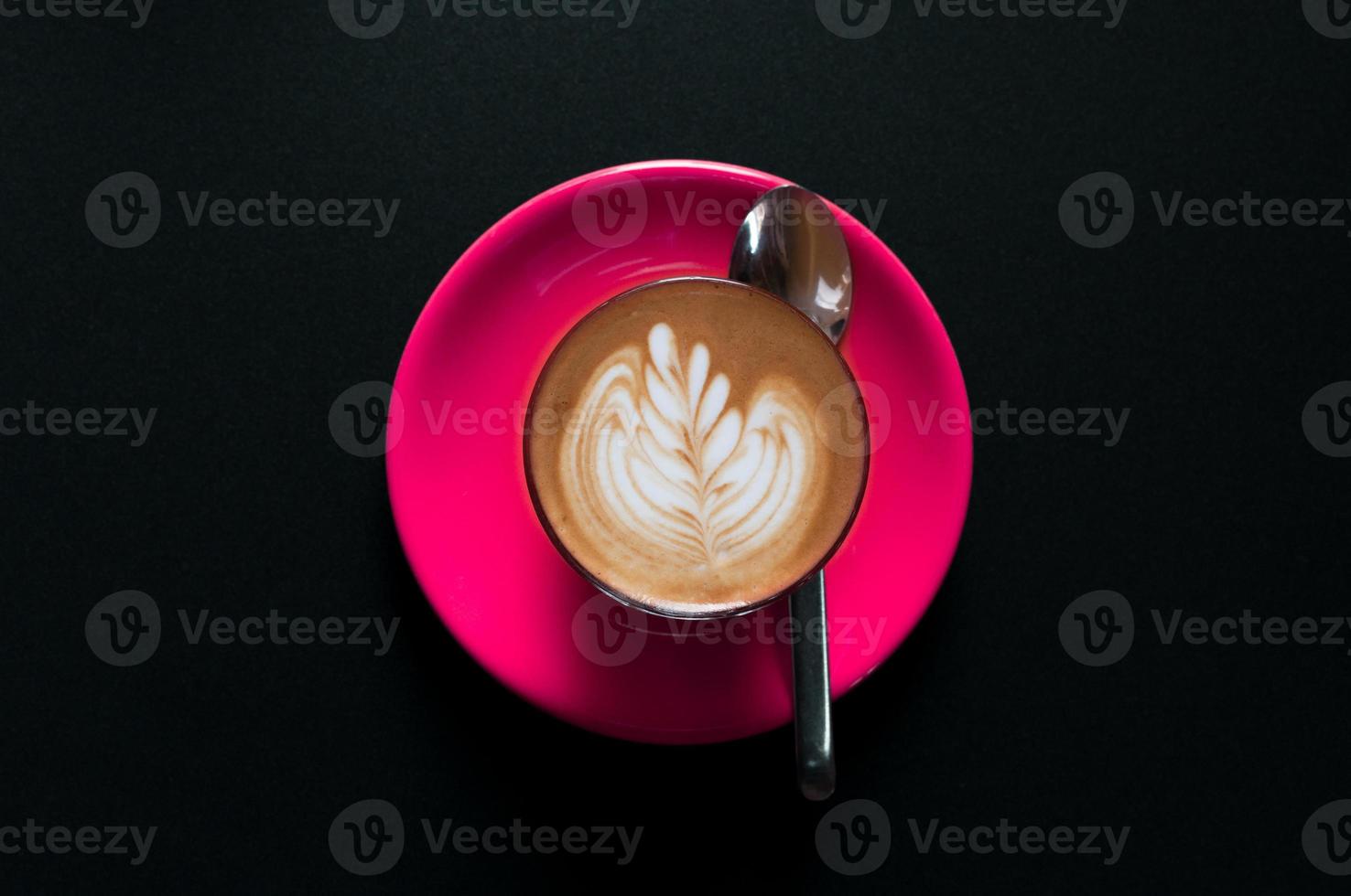 Hot latte in pink cup with floral pattern in foam top view on a dark background photo