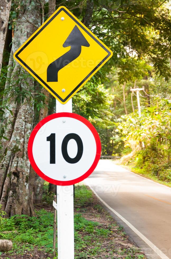 Selective speed limit traffic sign 10 and winding road caution symbol for safety drive in country road in mountain view forest,low key photo