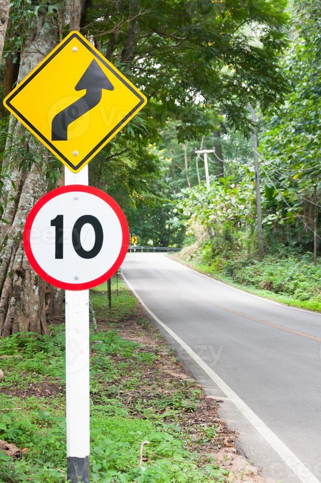 Selective speed limit traffic sign 10 and winding road caution symbol for safety drive in country road in mountain view forest,low key photo