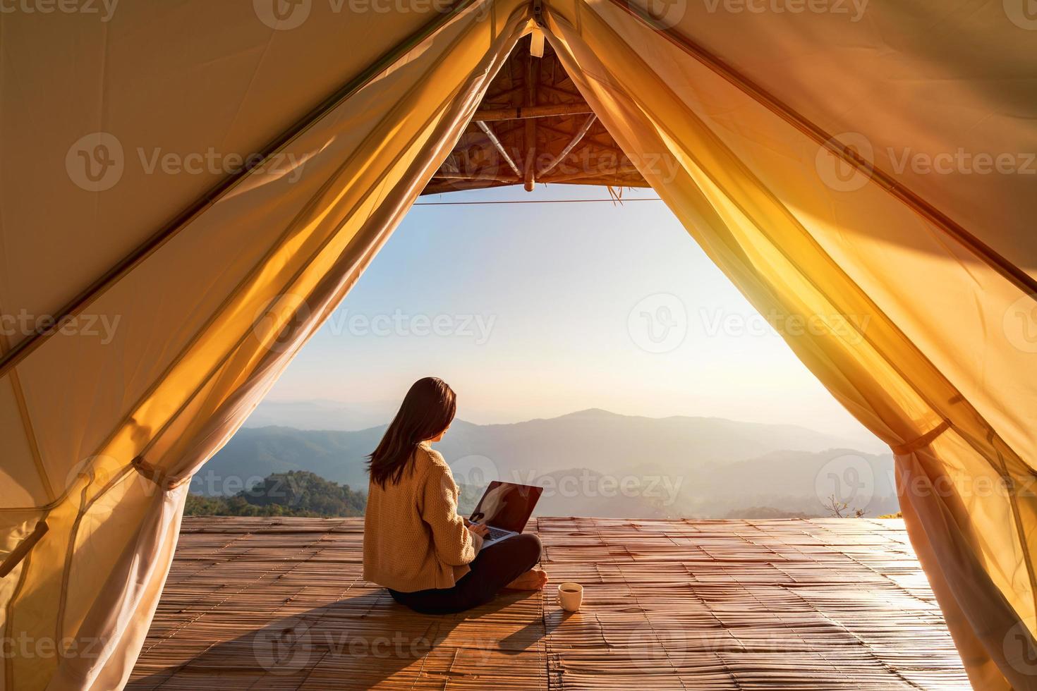 joven viajera independiente que trabaja en línea usando una computadora portátil y disfrutando del hermoso paisaje natural con vista a la montaña al amanecer foto