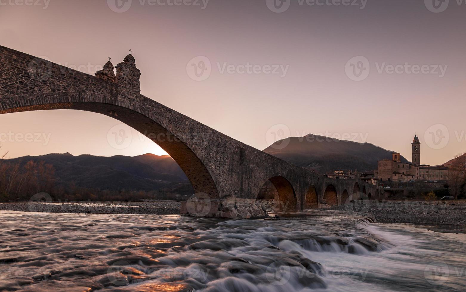 paisaje de un medieval puente terminado un turbulento río a puesta de sol foto