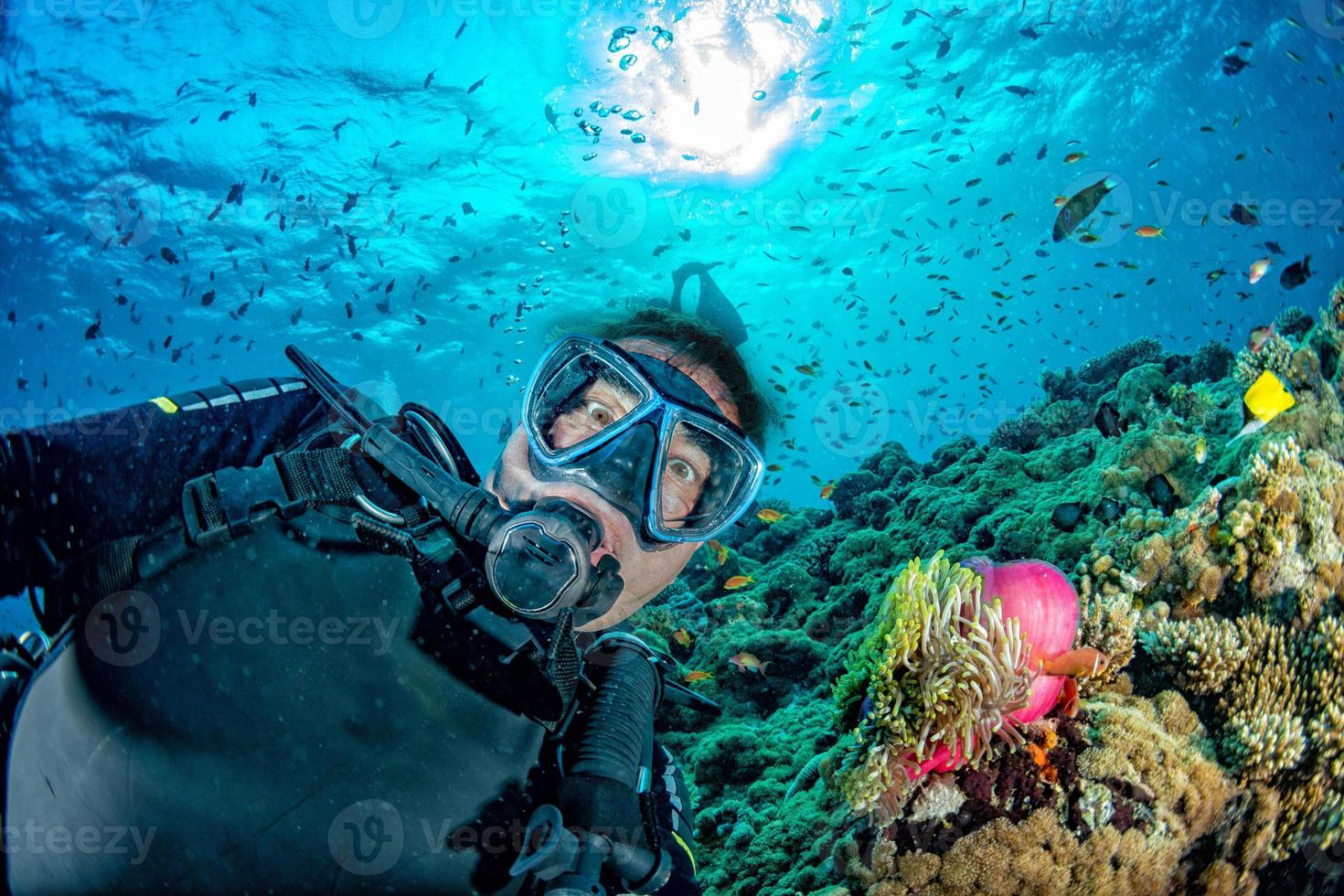 funny Scuba diver selfie in blue ocean backlight sun with Clown fish inside anemone photo