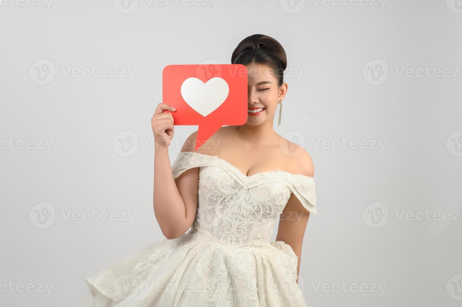 Asian beautiful bride smiling and posing with heart sign on white background photo