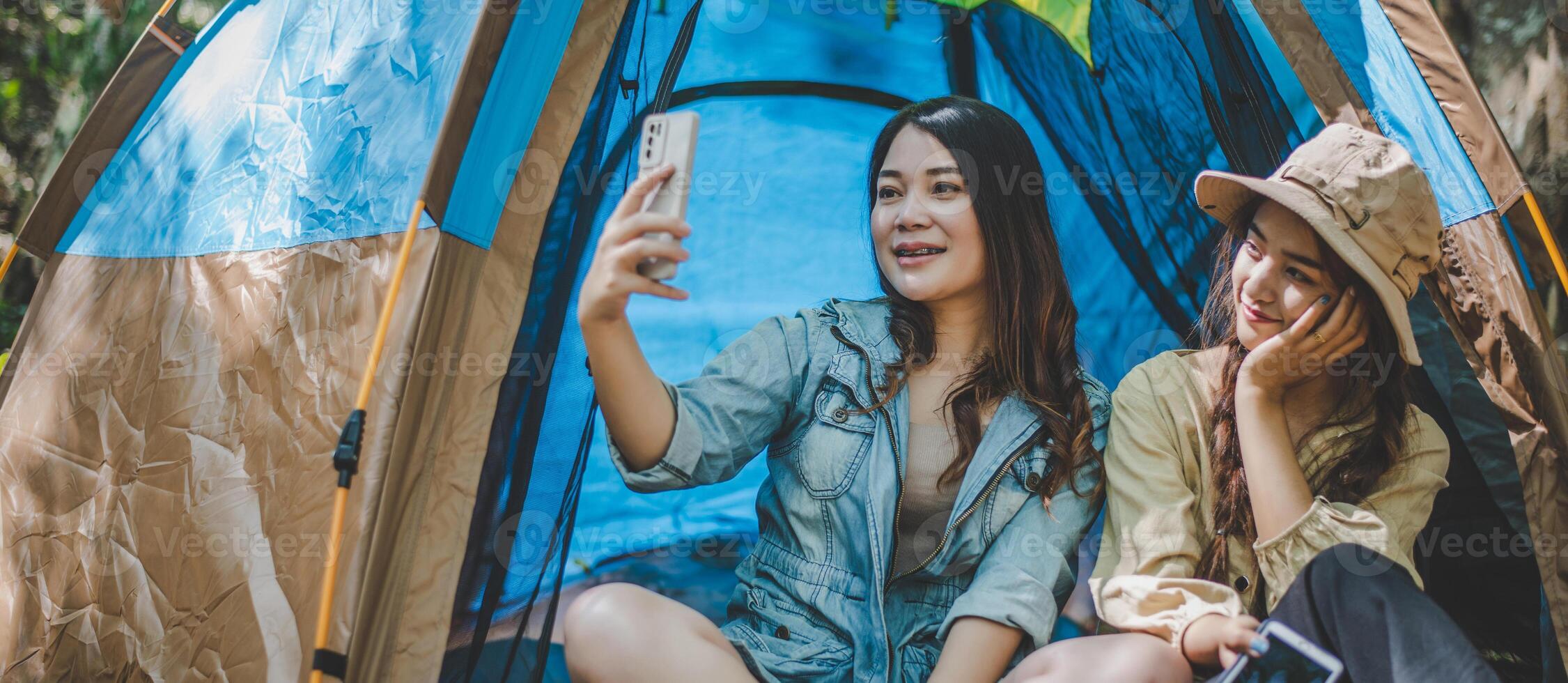 Asian pretty woman and friend use smartphone selfie on camping photo