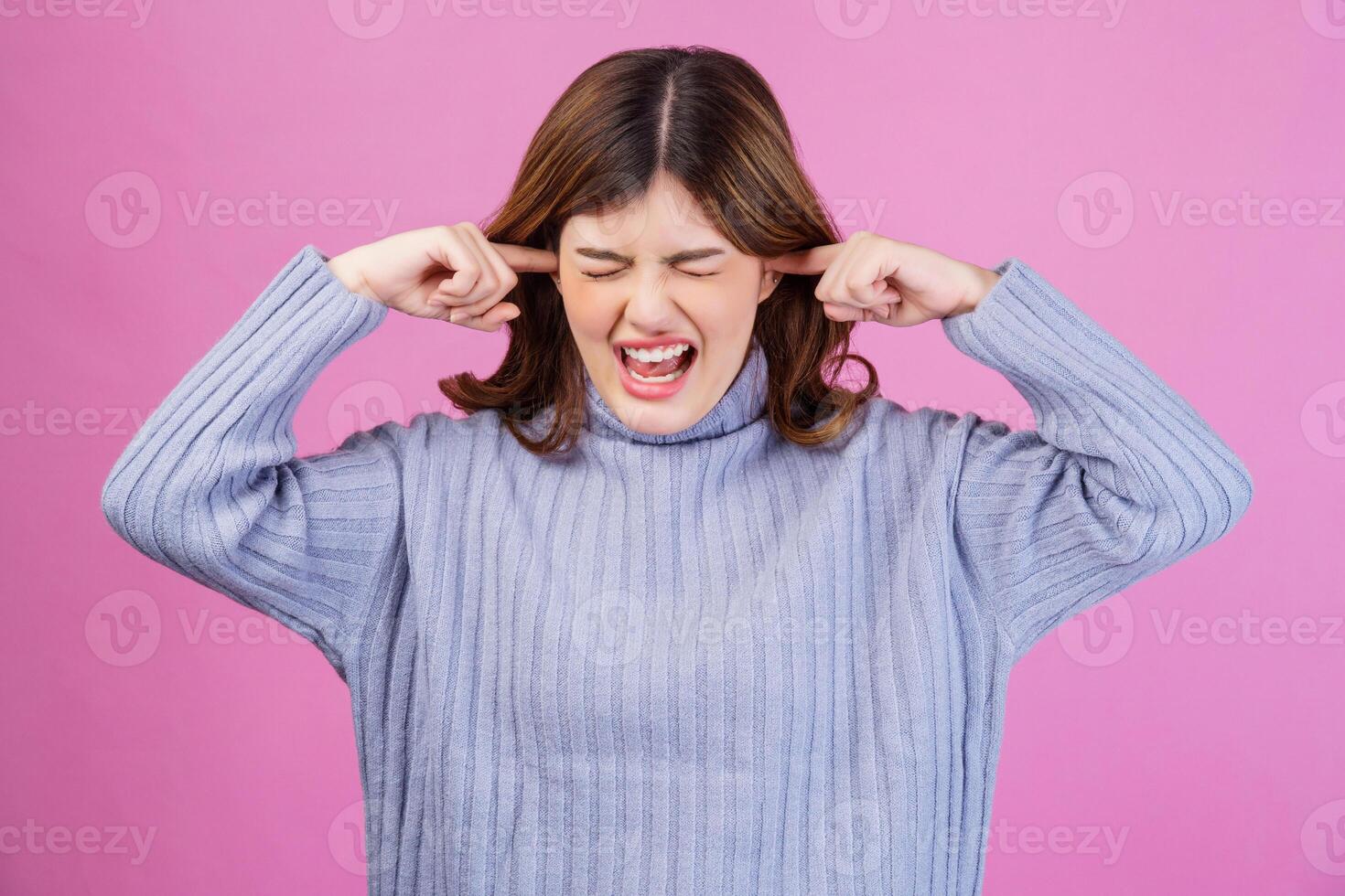 Portrait of Annoyed woman sticking plug fingers in ears not listening to loud noise sound isolated over pink background photo