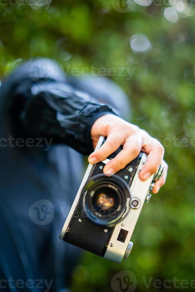 film camera in the hands of a girl taking a picture. Green trees boudoir backdrop.woman taking photos with a camera, selective focus, soft focus.
