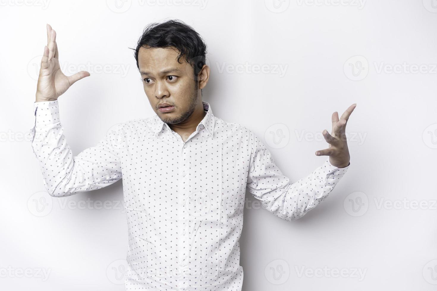 A portrait of an Asian man wearing a white shirt looks so confused between choices, isolated by a white background photo