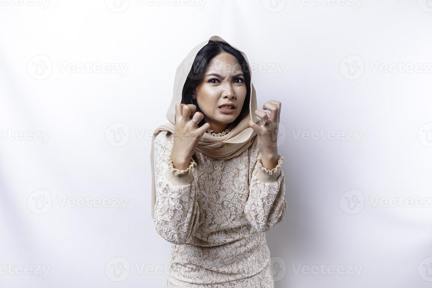 A dissatisfied young Asian Muslim woman looks at the camera posing on a white background, disgruntled girl with irritated face expressions show negative attitude photo