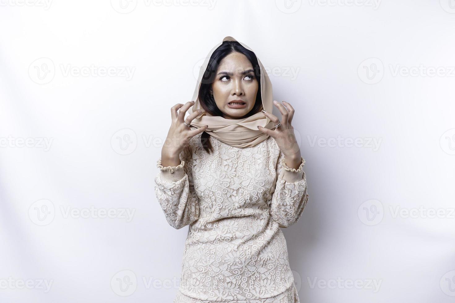 A dissatisfied young Asian Muslim woman looks at the camera posing on a white background, disgruntled girl with irritated face expressions show negative attitude photo