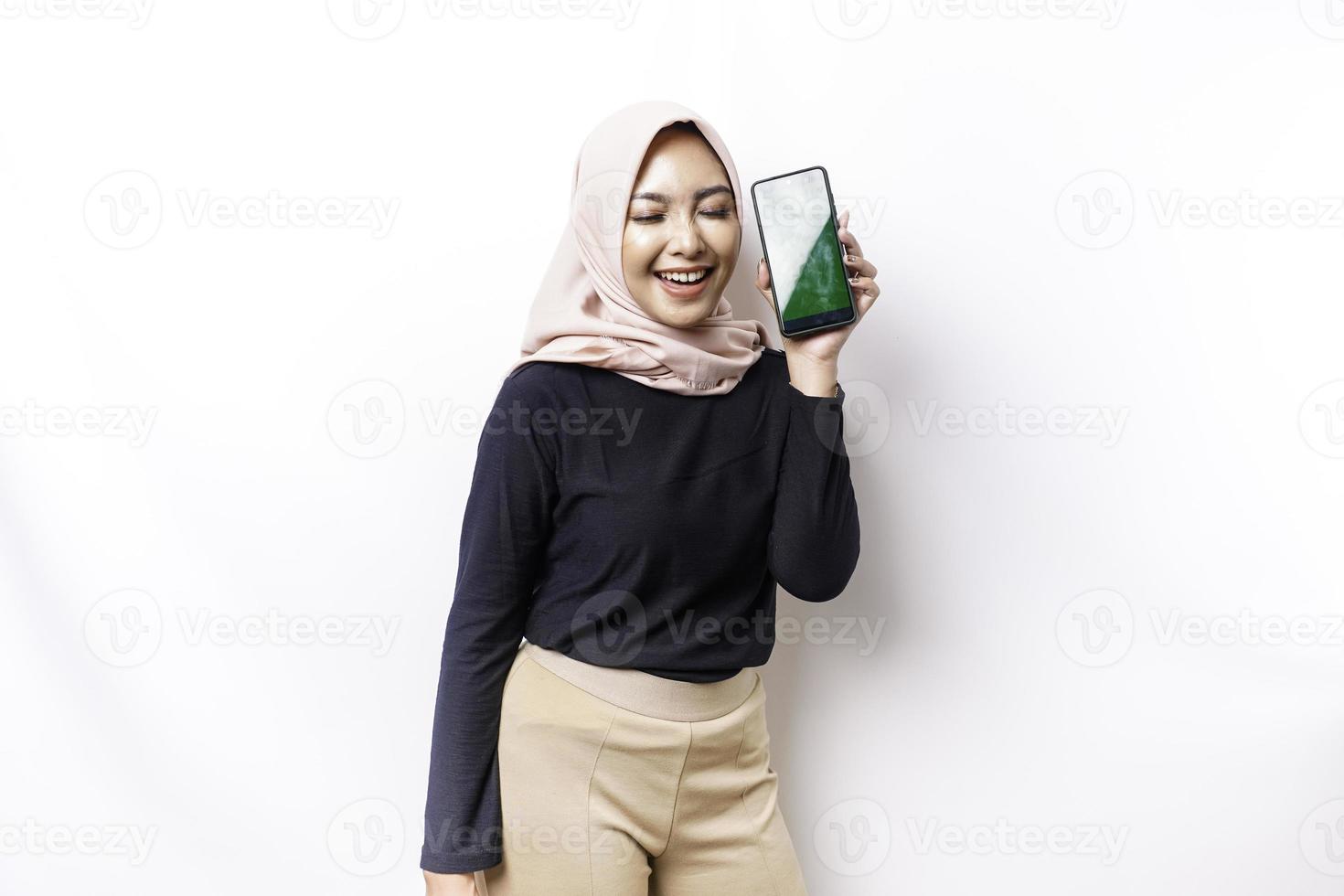 A portrait of a happy Asian Muslim woman wearing a hijab, showing her phone screen, isolated by white background photo