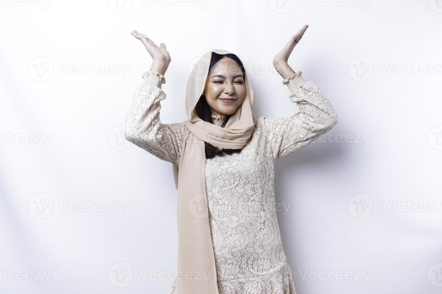 Excited Asian Muslim woman wearing hijab pointing at the copy space above her, isolated by white background photo