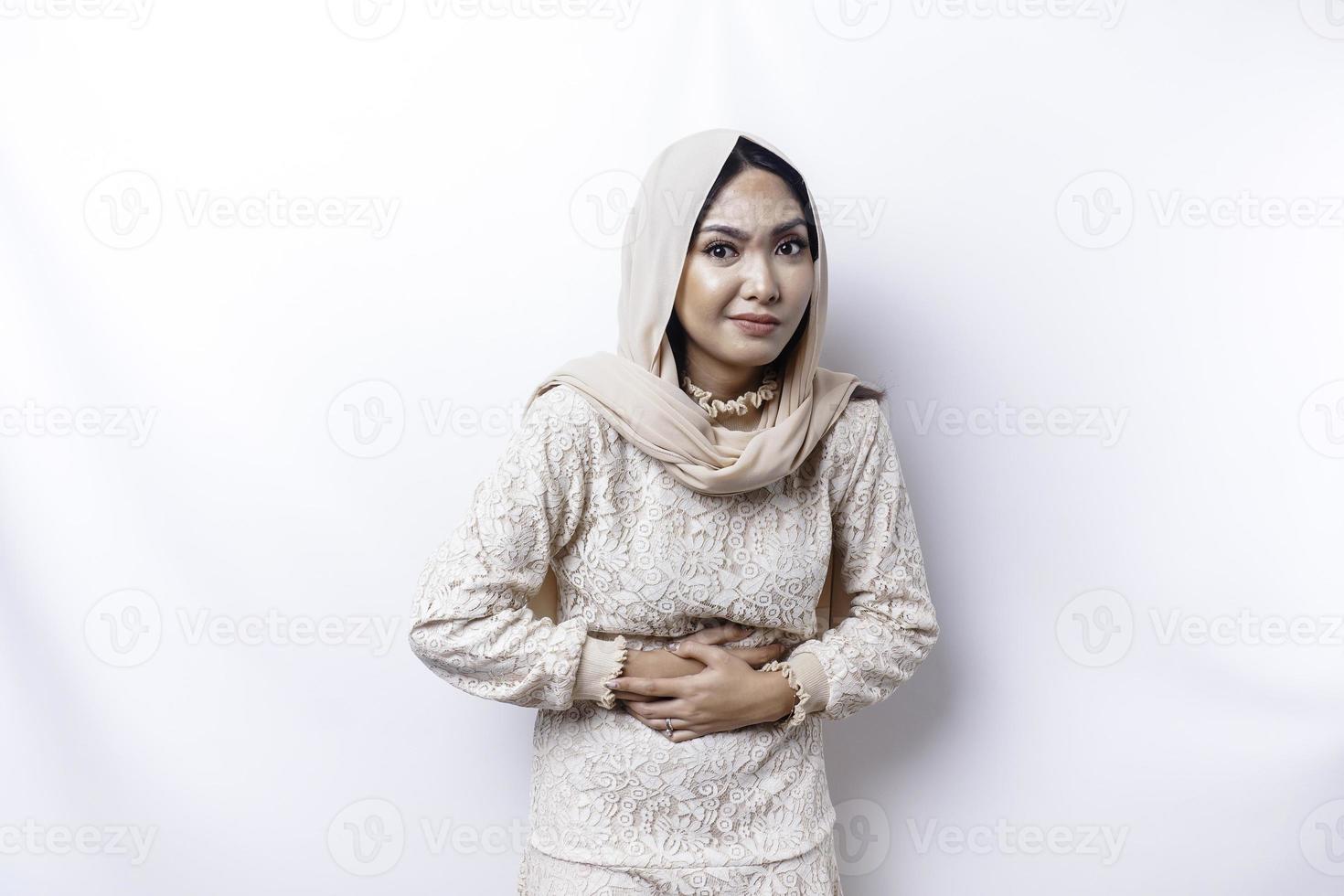 An Asian Muslim woman is fasting and hungry and touching her belly while looking aside thinking about what to eat photo