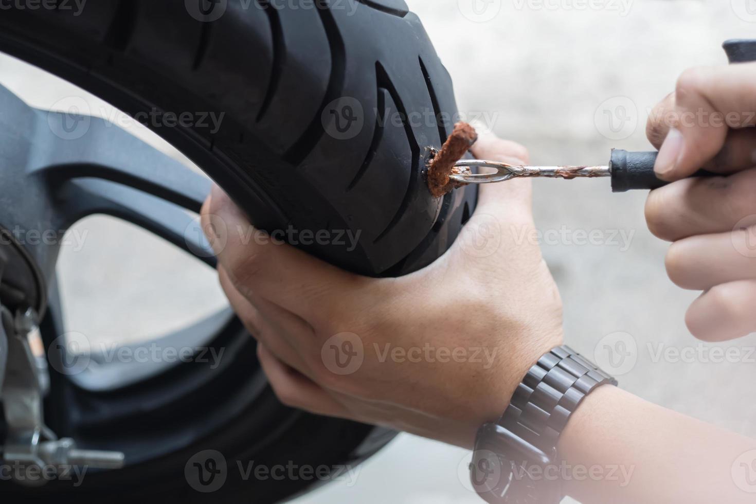 Rider use a tire plug kit and trying to fix a hole in tire sidewall ,Repair a motorcycle flat tire in the garage. motorcycle maintenance and repair concept photo