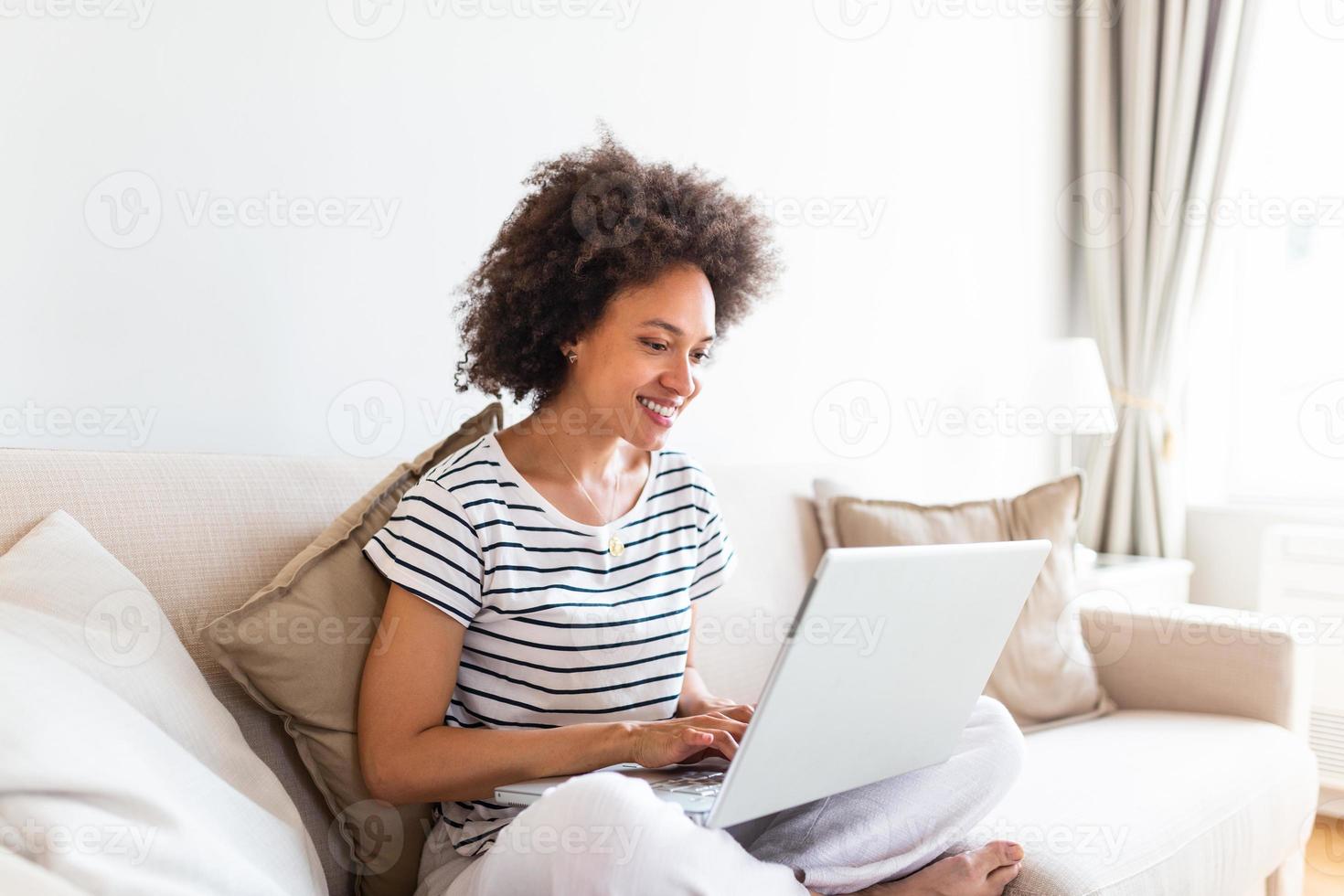 Young beautiful woman with curly hair working on laptop computer while sitting on the sofa at home, heck on oline shops for cyber monday sales. Technology woman concept alternative office freelance photo