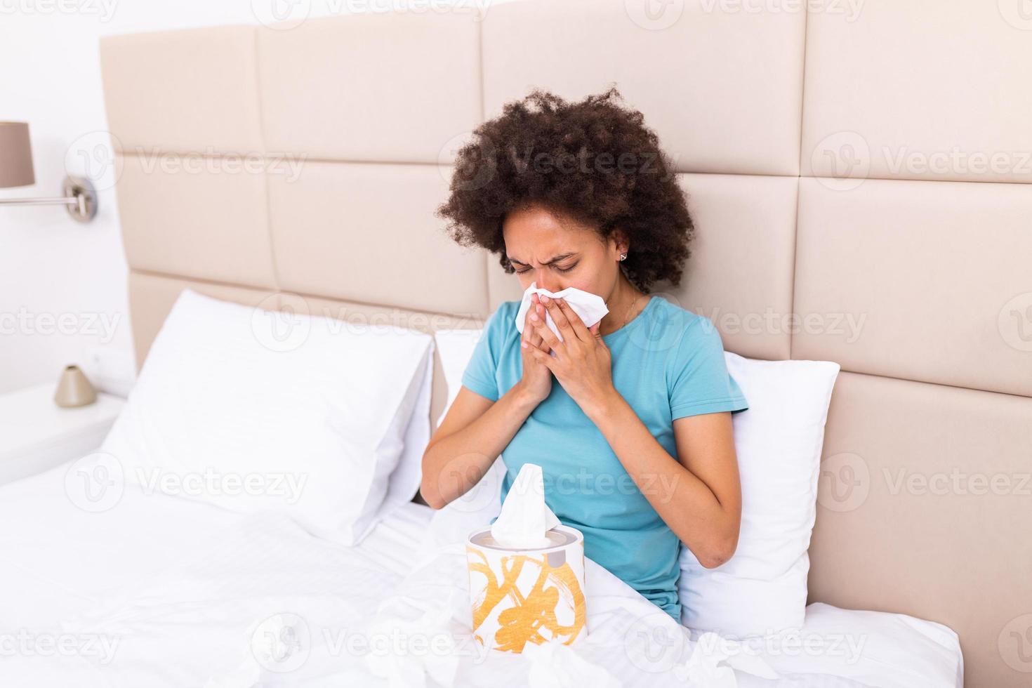 Sick black millennial girl sit on bed feel unhealthy blowing running nose, ill african American young woman suffering from rhinitis snuffles, having respiratory infection, get flue need medication photo