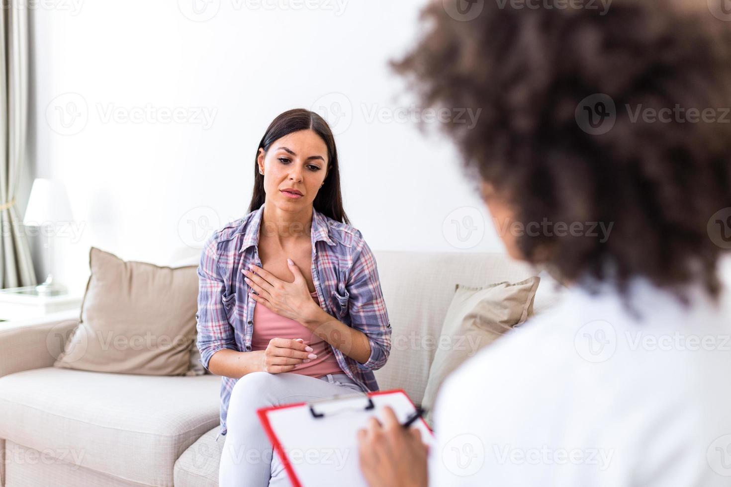 Young woman sitting on the sofa covering her chest with hands, feeling hopeless, depressed or crying, visiting psychotherapist, finding out bad diagnosis or medical test results photo