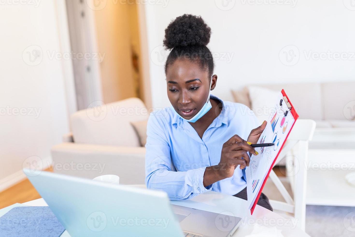 African american businesswoman having video conference while in quarantine during COVID-19 pandemic. Analyzing stock market chart and key performance indicators via video call photo